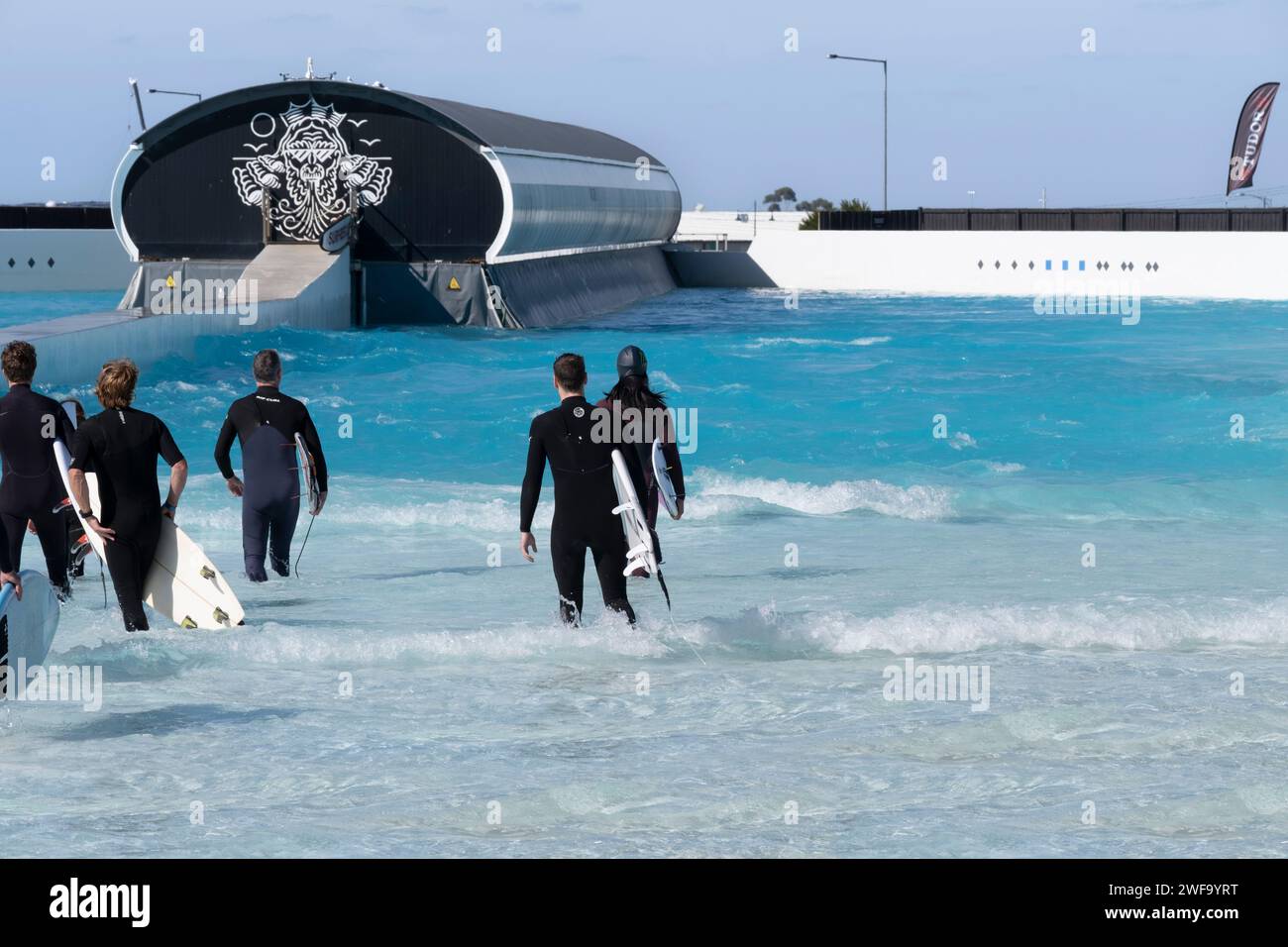 Les gens marchent dans l'eau avec leurs planches de surf sous les bras à Urbnsurf, la première piscine à vagues commerciale d'Australie à Melbourne Banque D'Images