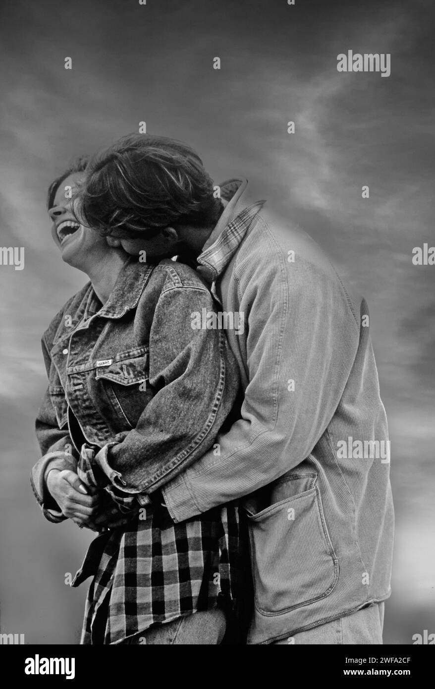 Photo en noir et blanc d'un couple souriant s'embrassant étroitement dans un parc, exprimant amour et affection. Banque D'Images