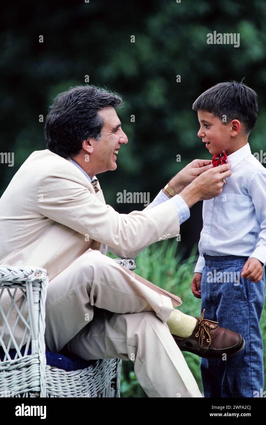 Un père vêtu d'un costume blanc aide son jeune fils à s'habiller avec un noeud papillon Banque D'Images