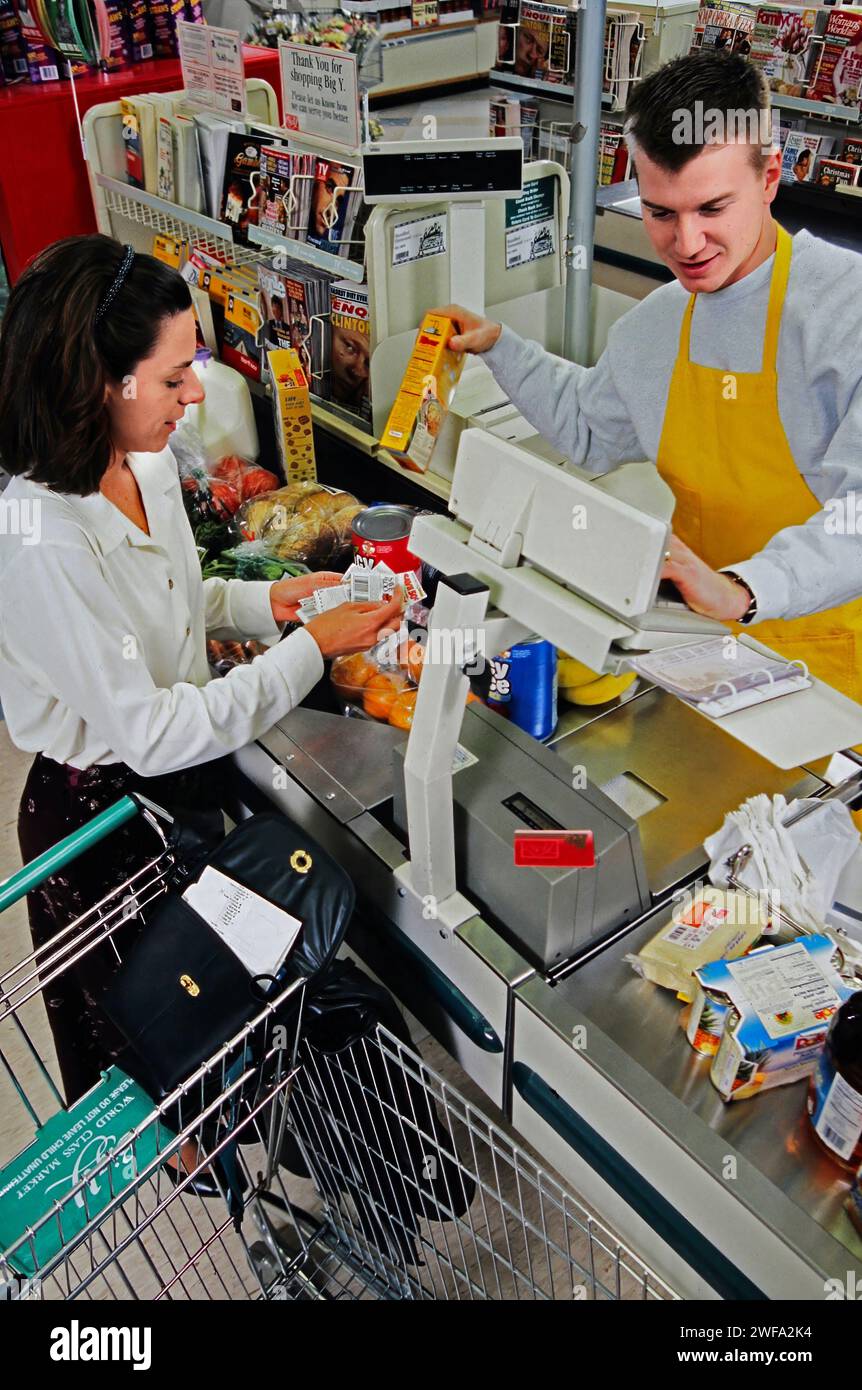 Check-out de supermarché avec un commis et un shopper stand à une caisse dans une épicerie achalandée, enregistrer les achats et gérer les transactions. Banque D'Images