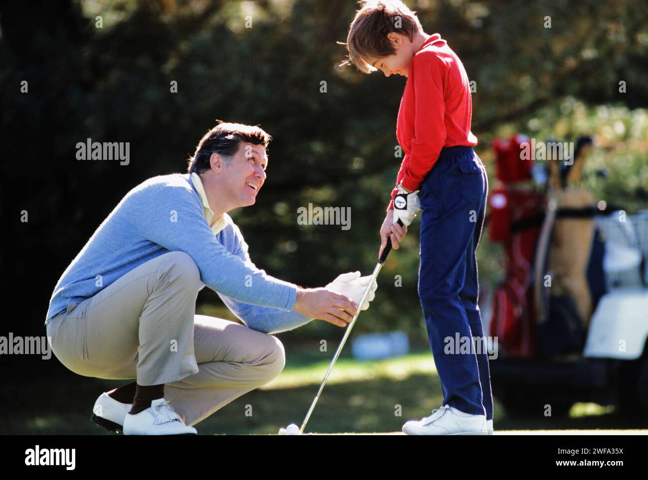 Un père enseignant à son fils non sur le jeu de golf sur un parcours verdoyant par une journée lumineuse et ensoleillée. Banque D'Images