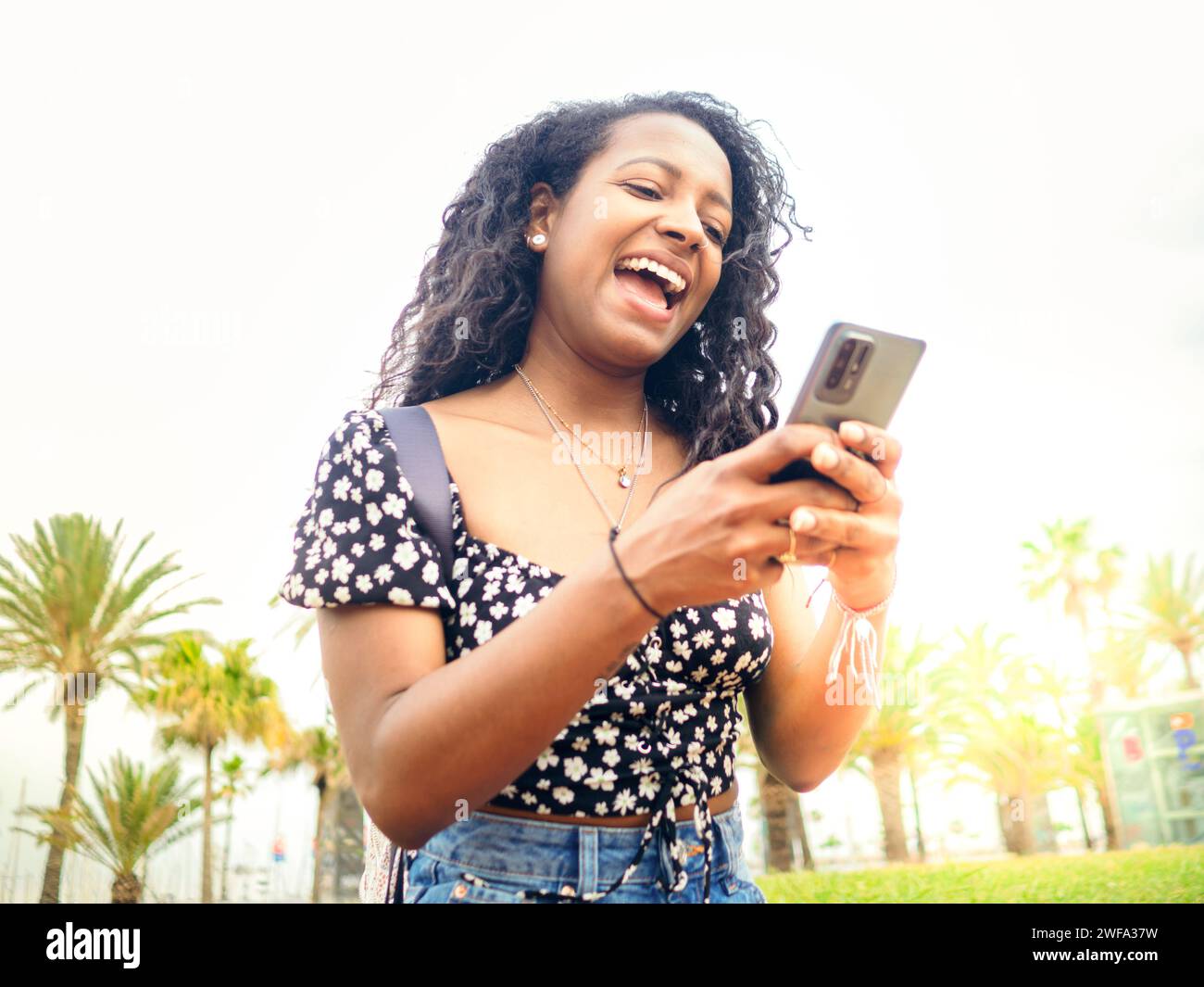 Heureuse jeune femme afro-américaine bavardant avec smartphone dans une ville pendant des vacances Banque D'Images