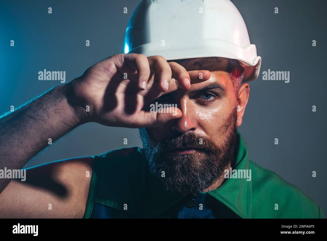 Portrait en gros plan de constructeur fatigué dans le casque de construction. Le travailleur fatigué essuie la sueur du front. Dur labeur sur le chantier de construction. Profession lourde Banque D'Images