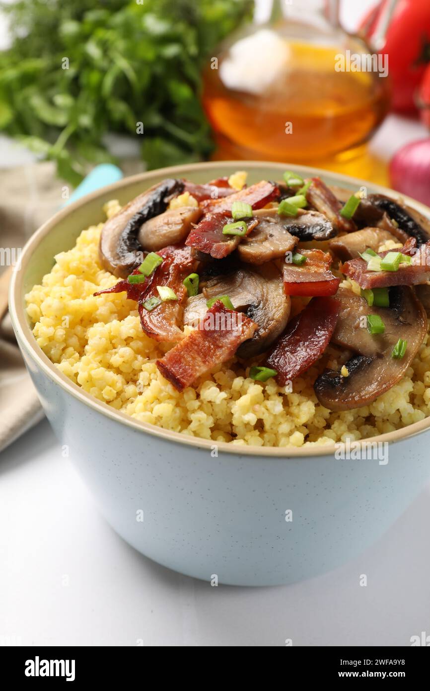 Savoureux porridge de millet avec des champignons, du bacon et de l'oignon vert dans un bol sur une table blanche, gros plan Banque D'Images