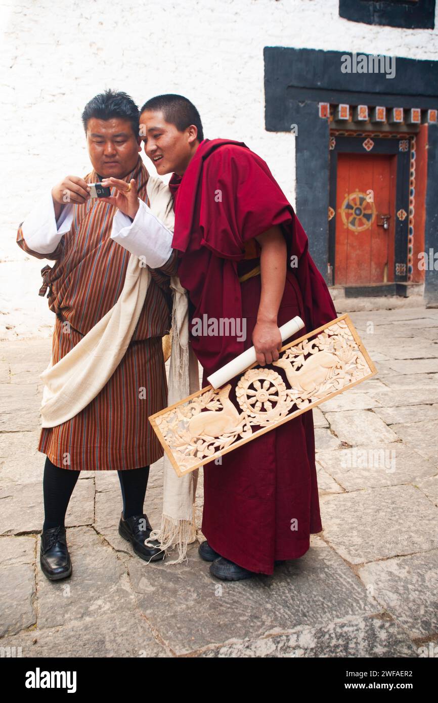 Moine en robe rouge et un bhoutanais portant un regard traditionnel gho à l'arrière de l'appareil photo numérique, Trongsa Dzong, Trongsa, centre du Bhoutan Banque D'Images