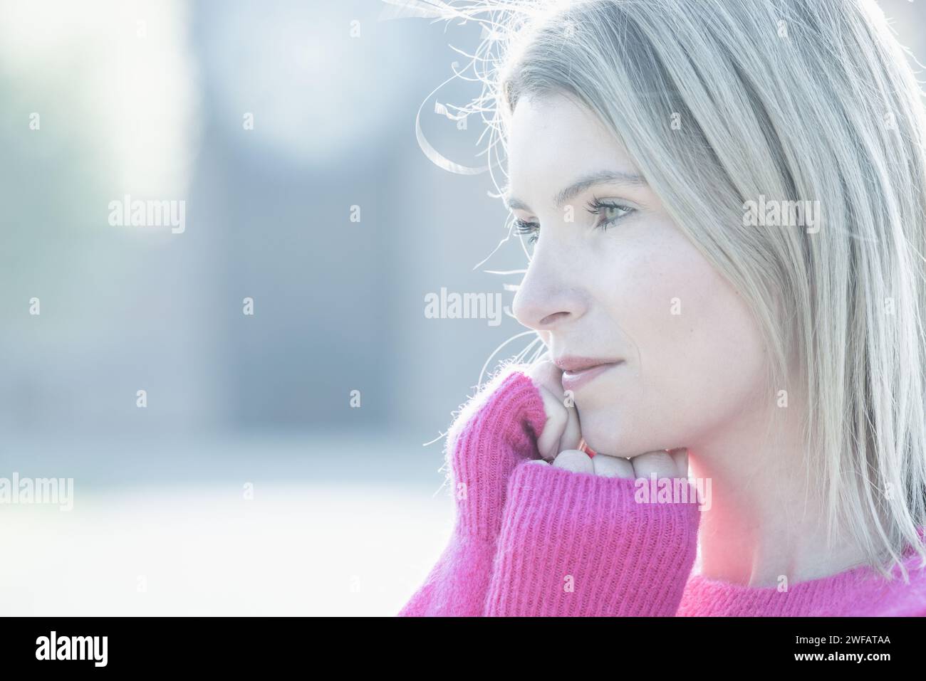 Le portrait en gros plan montre une jeune femme caucasienne dans un pull rose pastel doux. L'image est baignée dans une lumière fraîche et diffuse, soulignant l'humeur pensive sur son visage. Son regard est dirigé hors caméra, suggérant une pensée profonde ou une réflexion. L’éclairage high-key accentue son teint clair et la texture fine du pull, tandis que le fond reste indistinct, soulignant son moment introspectif. Ambiance pensive en rose pastel. Photo de haute qualité Banque D'Images