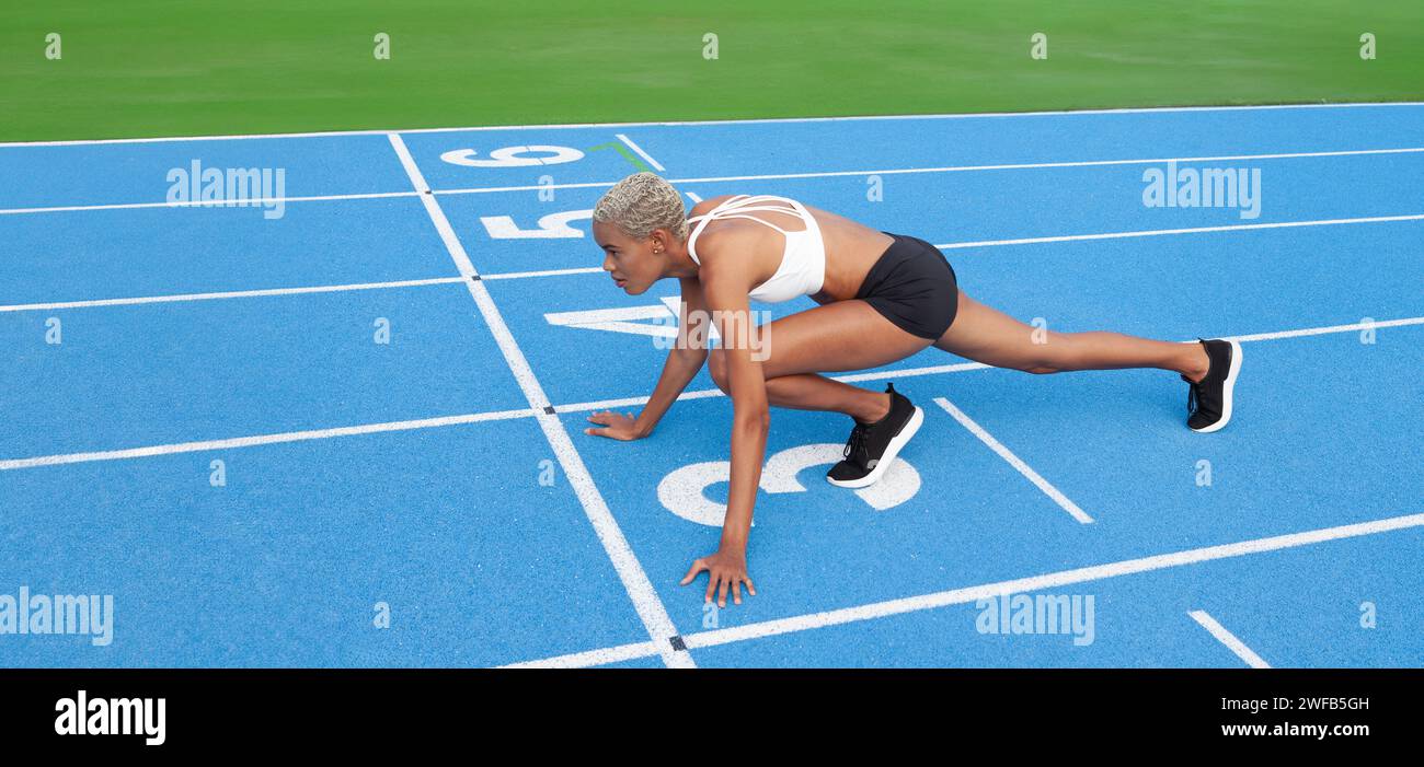 Une athlète afro-américaine se tient prête à la ligne de départ sur la piste bleue olympique, incarnant le concept d'entraînement et de dévouement à la course Banque D'Images