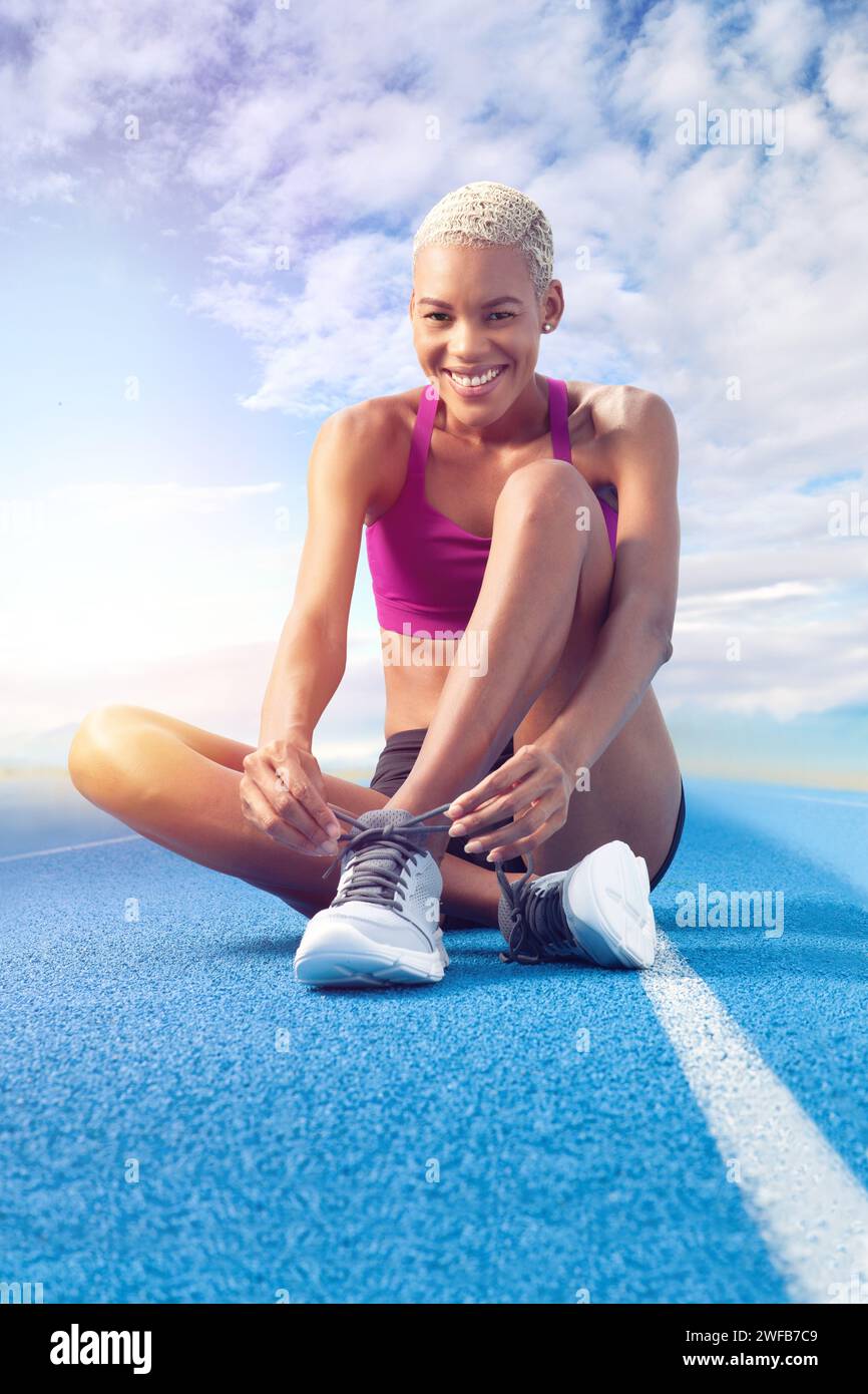 Une athlète afro-américaine, femme souriante lacet ses chaussures assis sur la piste bleue olympique, incarnant le concept de course d'entraînement et dé Banque D'Images