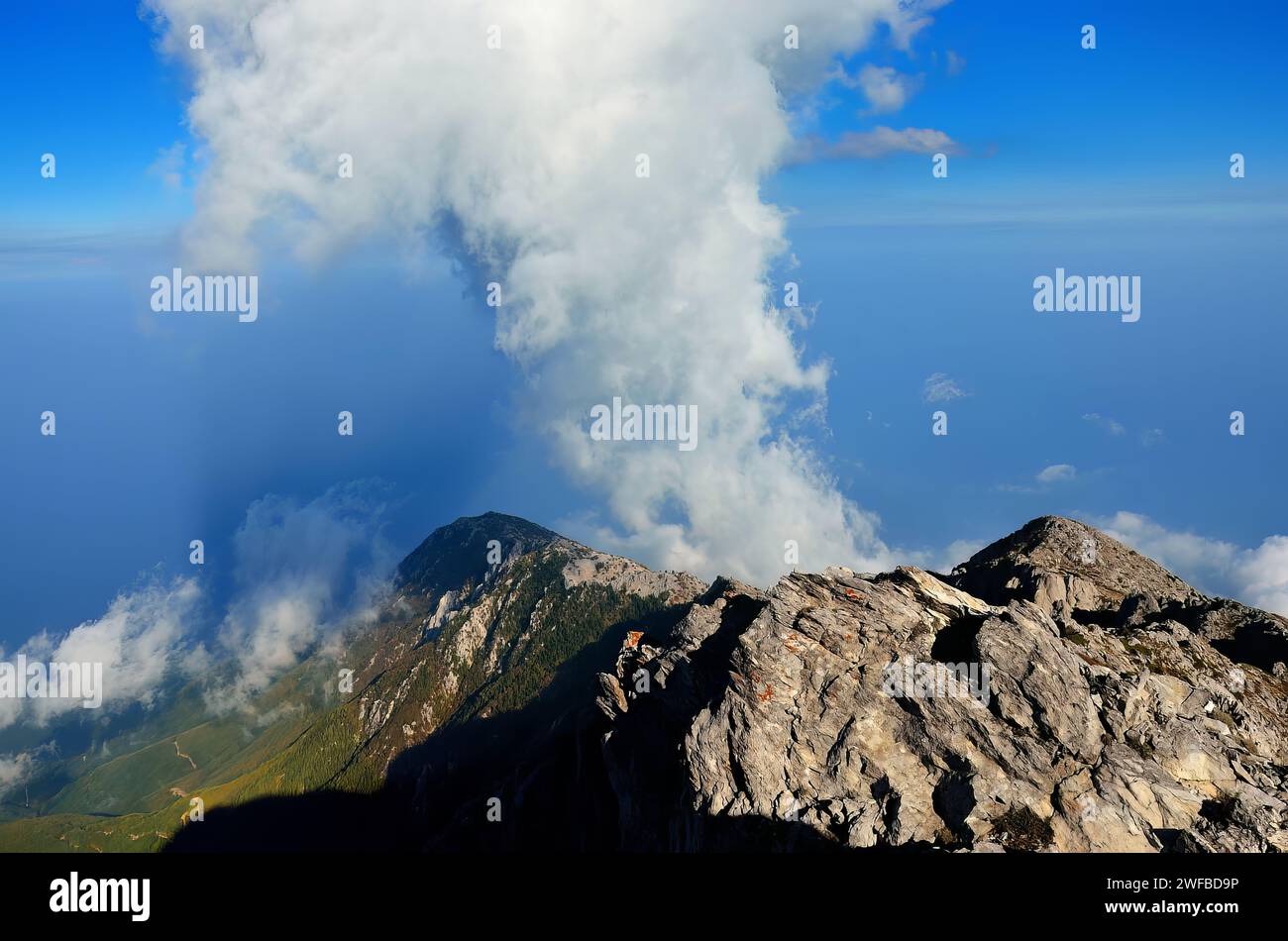 Un paysage pittoresque d'une colline ornée de nombreuses montagnes majestueuses et de nuages, surmonté d'un petit nuage blanc distinctif Banque D'Images