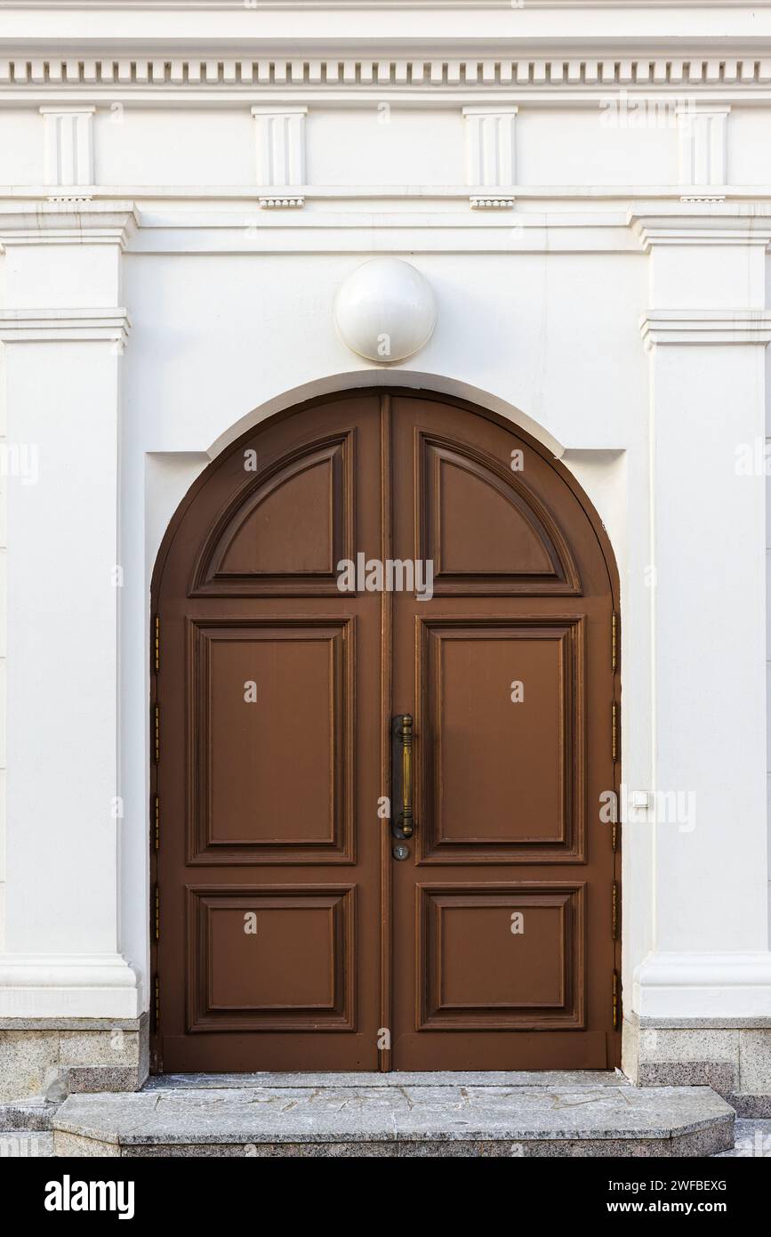 Porte voûtée en bois brun dans le mur blanc avec des détails de décoration d'architecture classique, vue de face, texture de photo de fond Banque D'Images