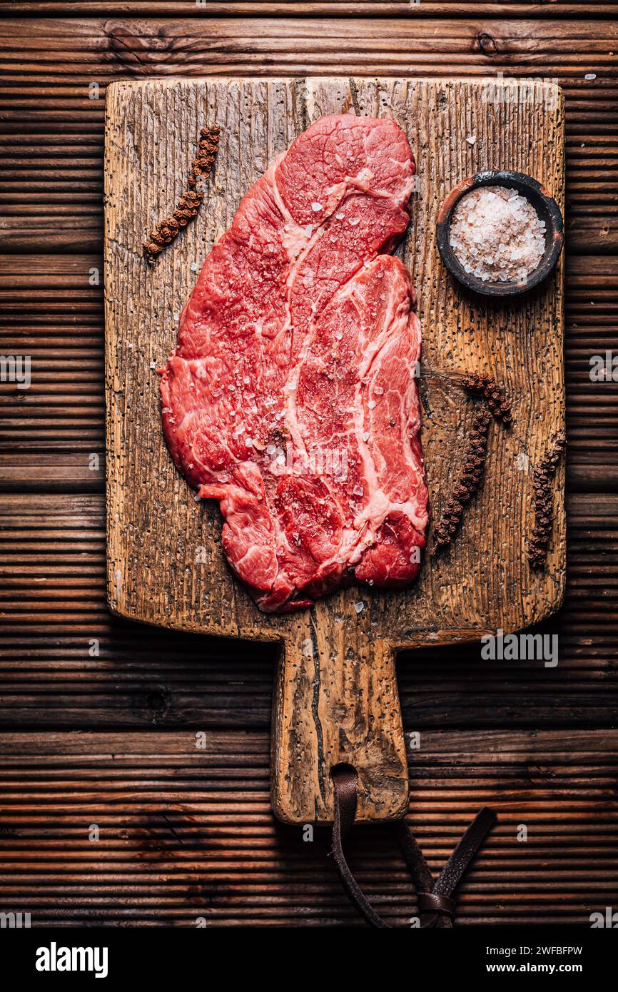 Steak de bœuf Chuck Eye cru assaisonné de sel et de poivre sur une planche à découper en bois Banque D'Images