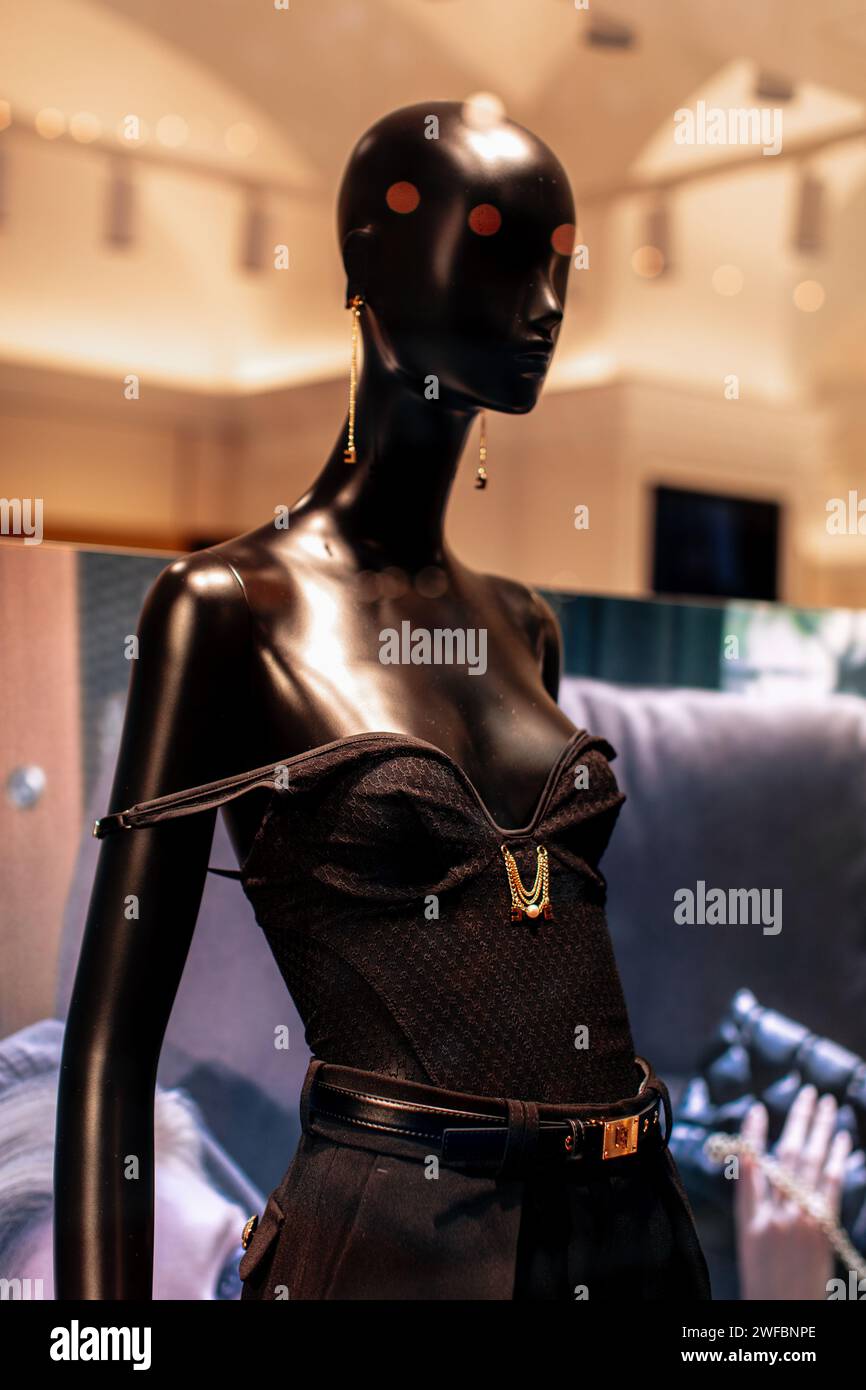 Mannequin élégant dans une fenêtre de boutique habillé d'un pantalon noir avec ceinture et tenant un petit sac à main en cuir Banque D'Images