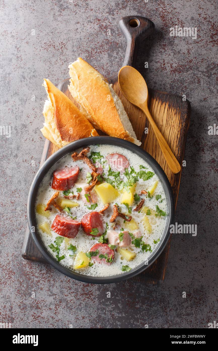 Borscht blanc polonais avec légumes, saucisse fumée, champignons séchés et bacon gros plan dans une assiette sur la table. Vue verticale de dessus Banque D'Images