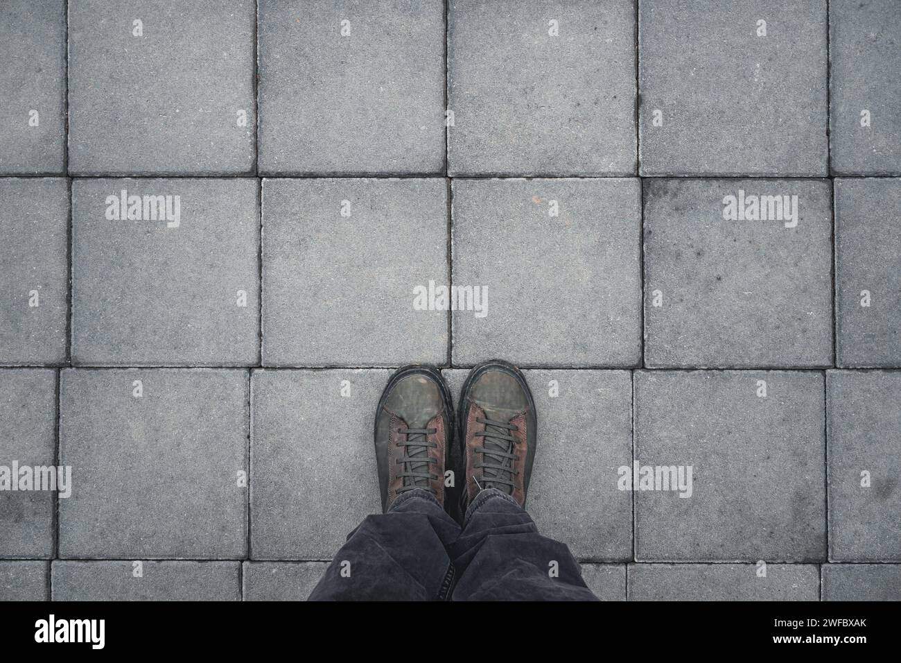 Homme debout sur les dalles de chaussée en béton de forme carrée, vue de dessus de bottes sales avec espace de copie Banque D'Images