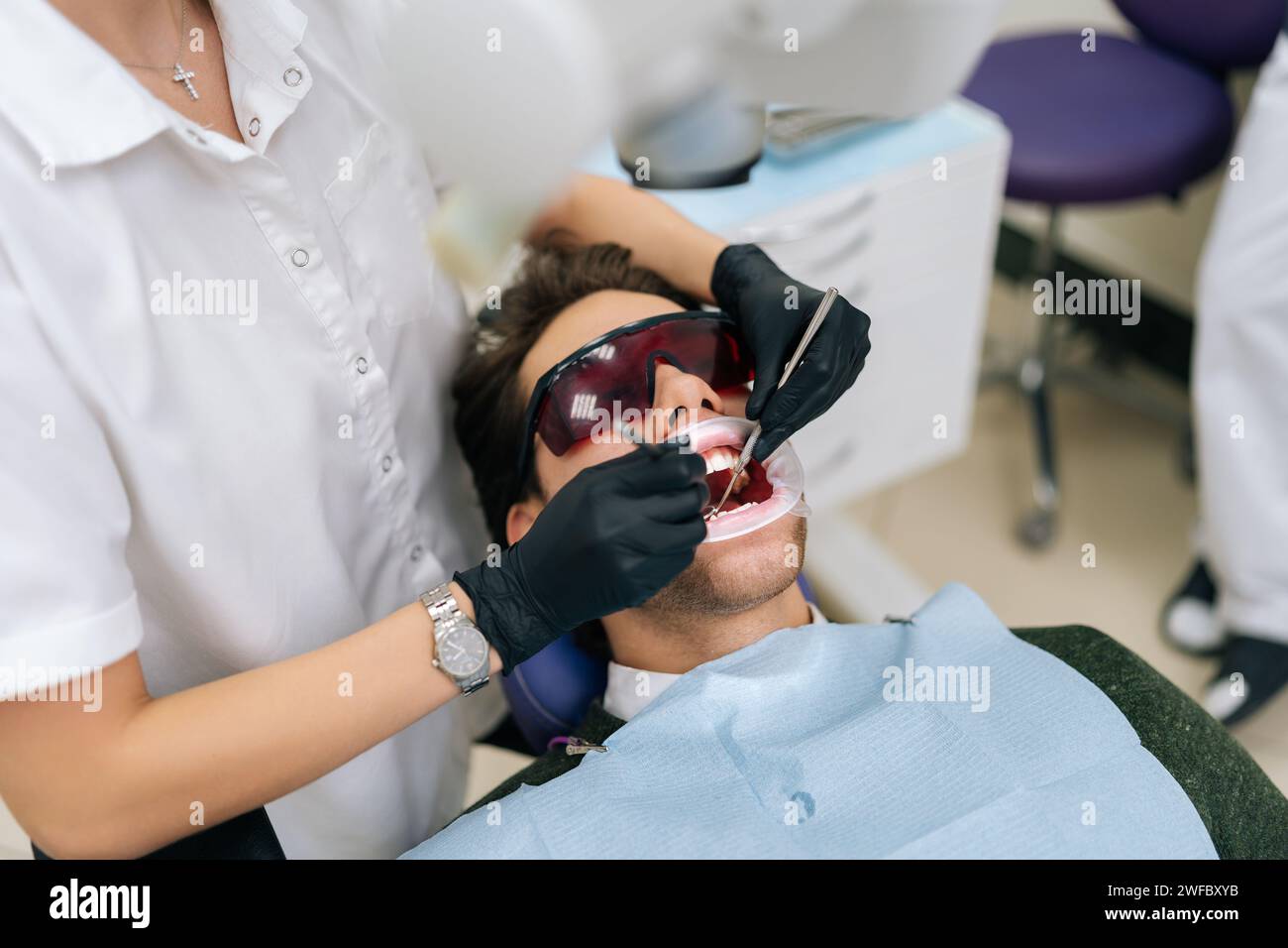Gros plan d'une dentiste méconnaissable utilisant le laser dentaire à diode moderne pour les soins parodontaux. Patient masculin portant des lunettes de protection, prévention Banque D'Images