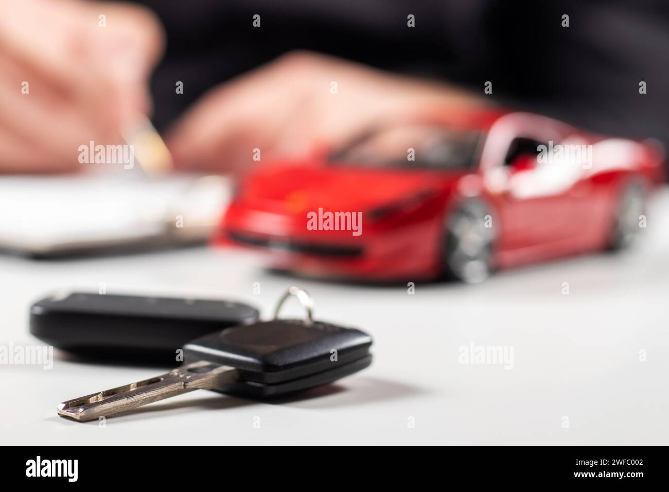 L'homme signe le document d'assurance automobile ou le papier de location. Signature écrite sur le contrat ou l'accord. Acheter ou vendre un véhicule neuf ou d'occasion. Touches de voiture sur l'onglet Banque D'Images