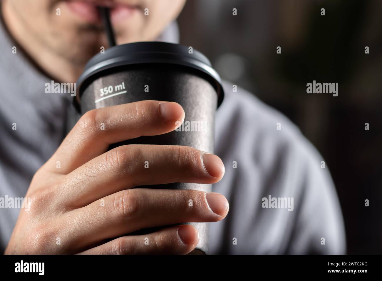 Homme buvant du café dans une tasse jetable avec un tube à cocktail en gros plan, Banque D'Images