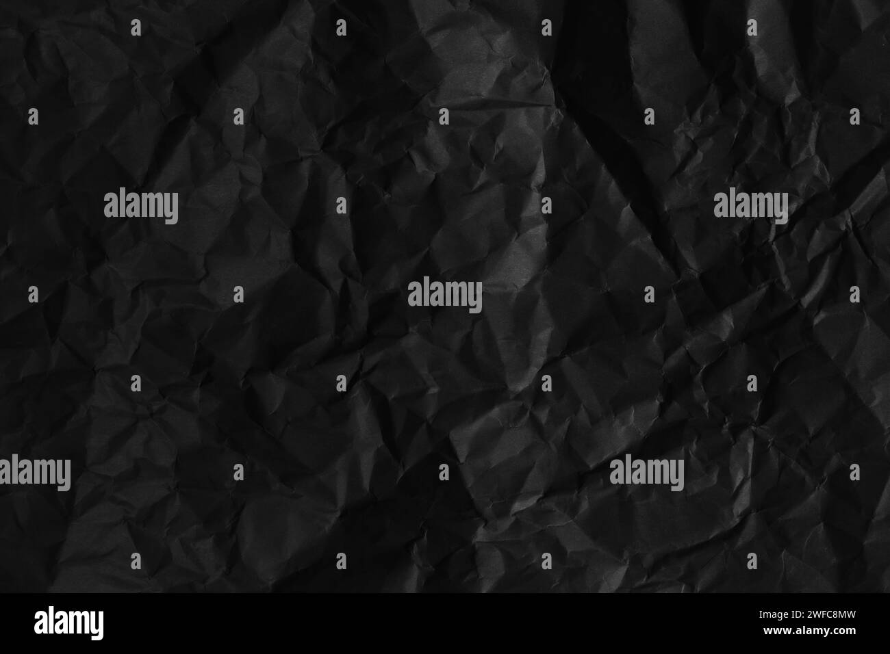 Texture de papier froissé noir sur fond faiblement éclairé. Banque D'Images
