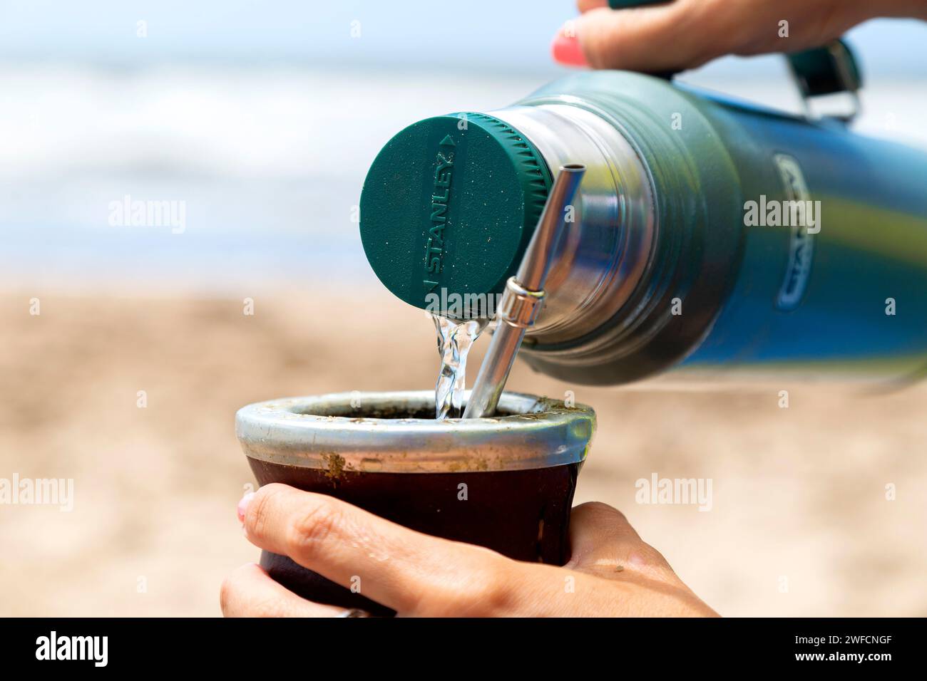 Femme servant l'eau chaude d'un thermos Stanley dans un Mate avec yerba. Boire Mate sur la plage. Mar Azul, Buenos Aires, Argentine - 25 janvier 2024. Banque D'Images