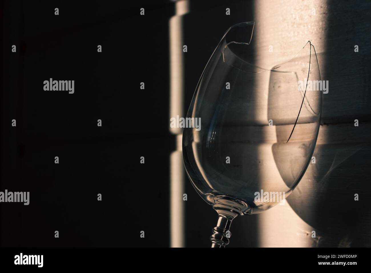 Verre à vin cassé dans la lumière du soleil sur fond en bois. Verre à vin endommagé avec bords tranchants. Verre fissuré dans les ombres. Nature morte créative. Objet fragile Banque D'Images