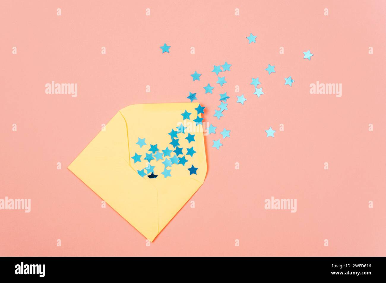 Enveloppe jaune avec des confettis bleus sur fond rose. Concept de vacances. Vue de dessus, pose à plat. Banque D'Images