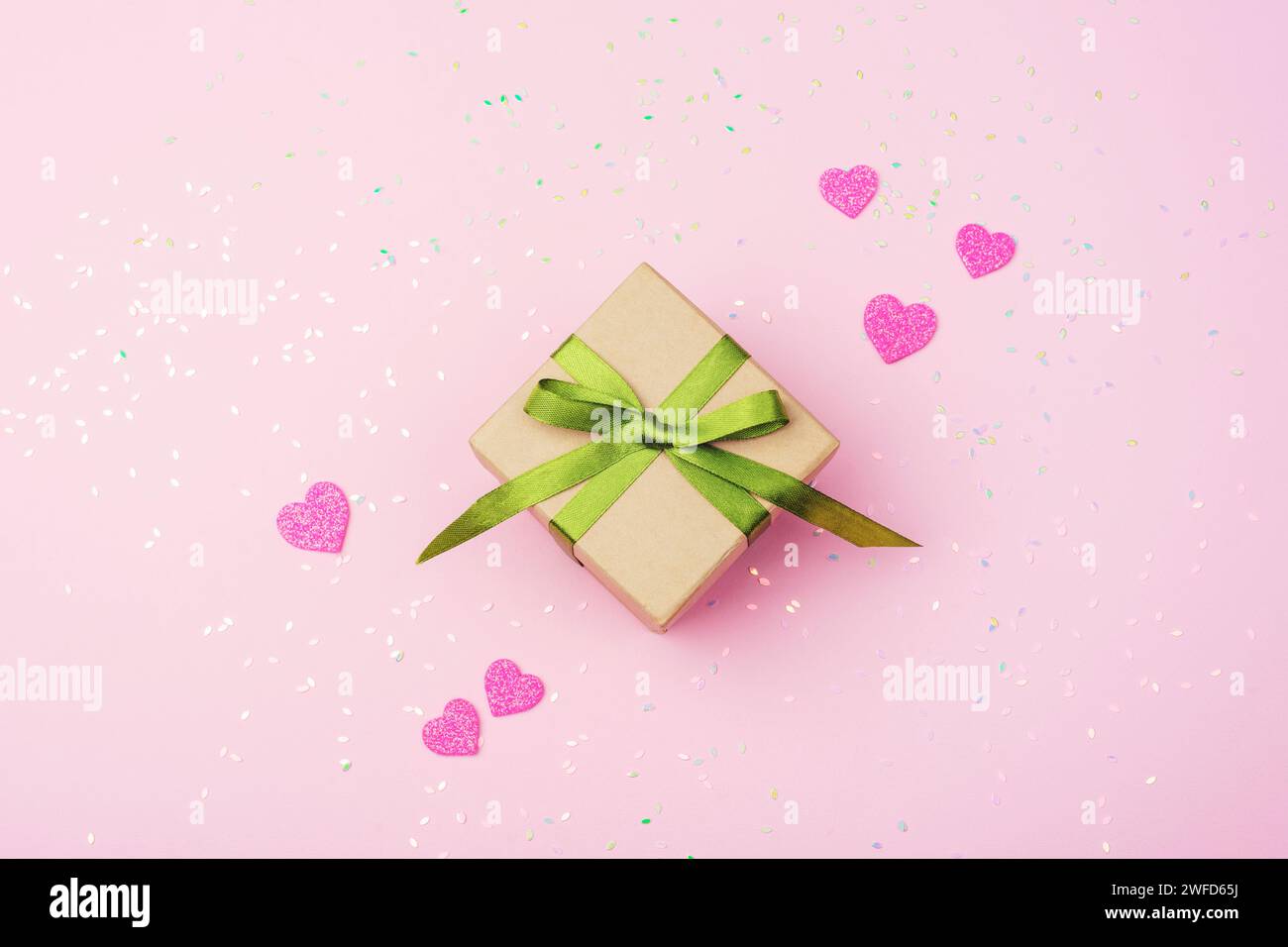 Boîte cadeau avec ruban vert, coeurs roses et décorations de confettis. Concept de Saint Valentin. Vue de dessus, pose à plat. Banque D'Images