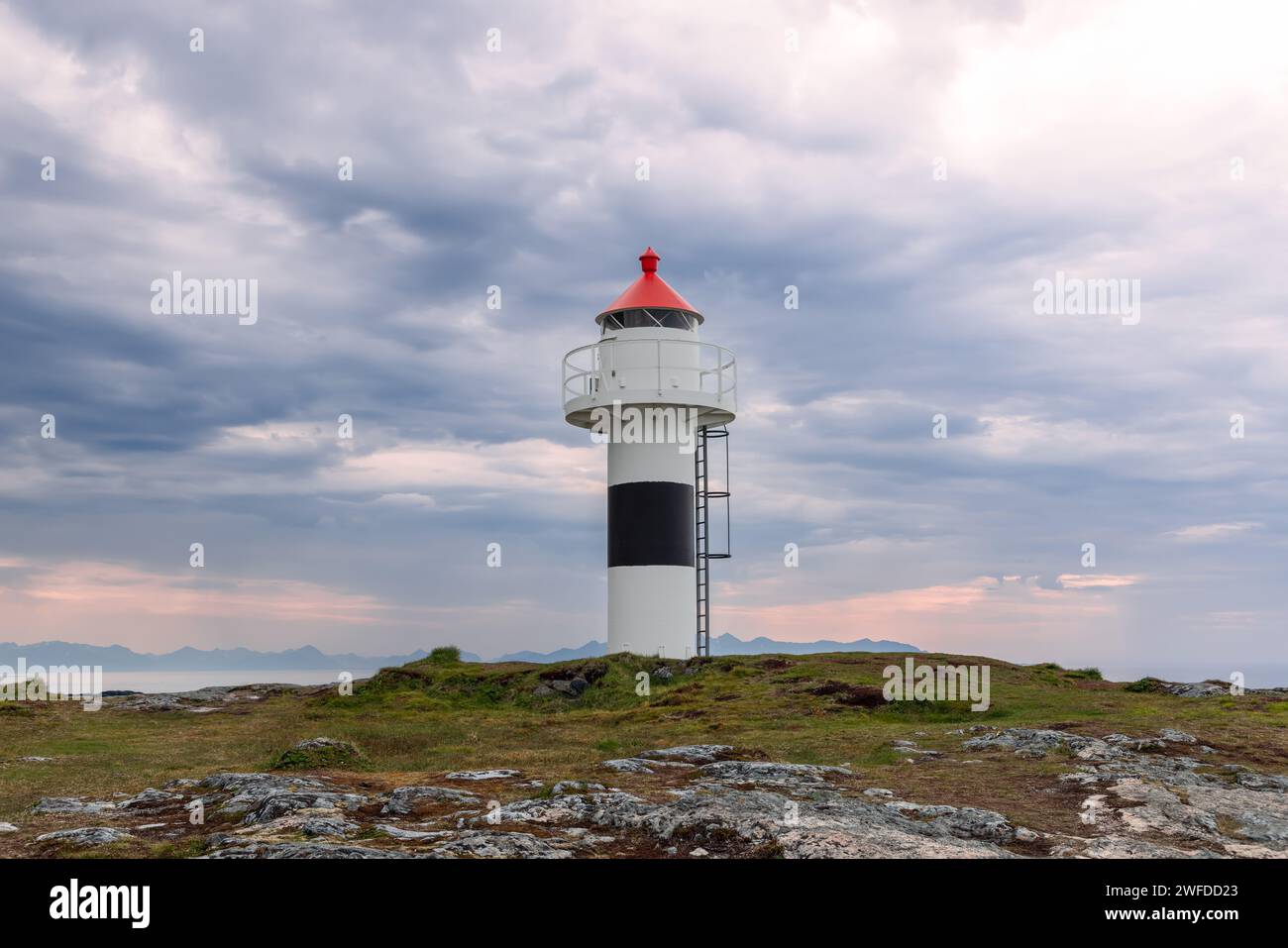 Le phare de Borhella se dresse face à un ciel spectaculaire, sa calotte rouge contraste fortement avec les nuages sombres au-dessus de la côte norvégienne Banque D'Images