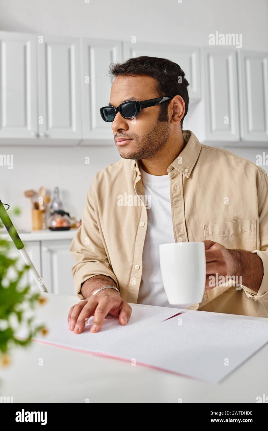 homme indien attrayant avec déficience visuelle dans les lunettes lisant le code braille pendant la cuisine Banque D'Images