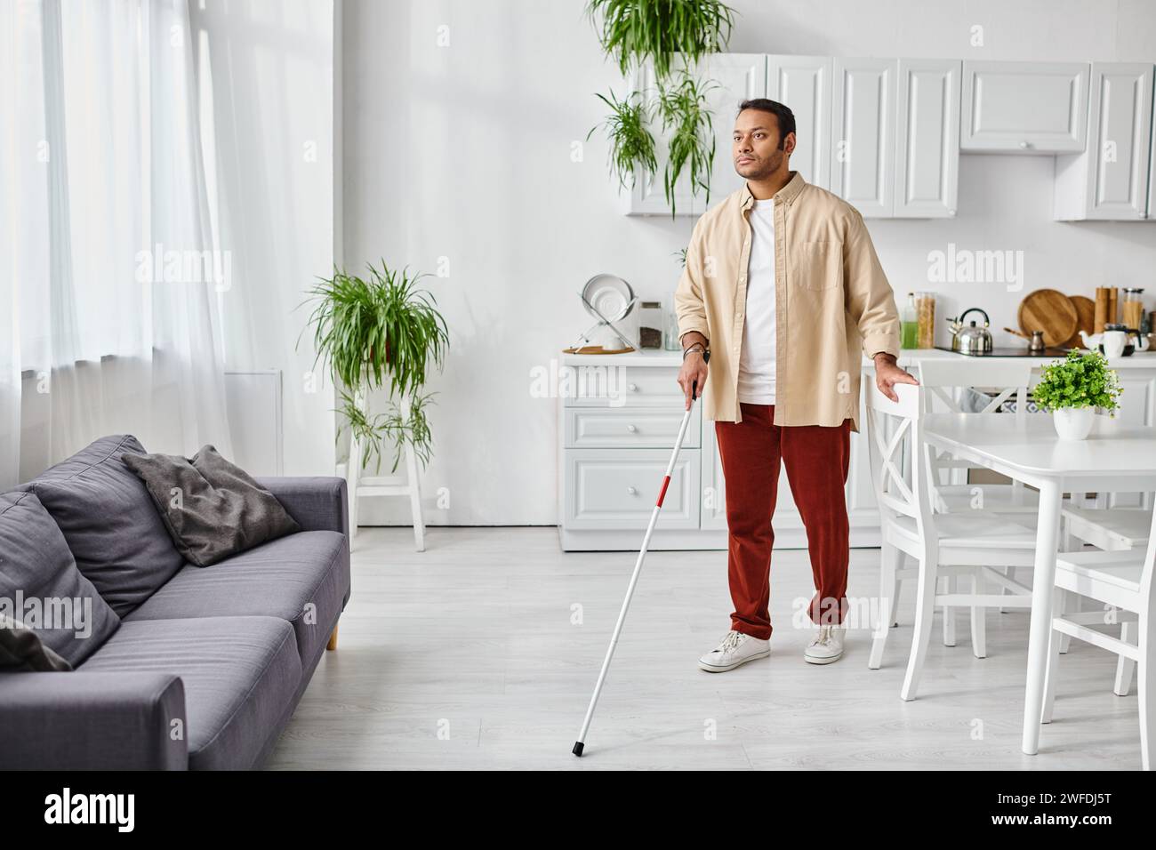 homme indien aveugle attrayant dans des vêtements de maison confortables décontractés utilisant le bâton de marche tandis qu'à la maison, handicapé Banque D'Images