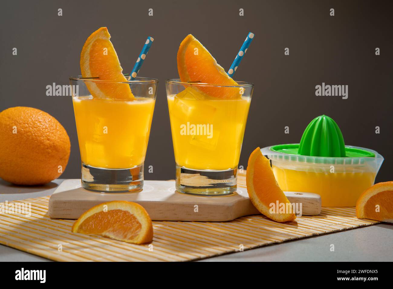 Deux cocktails jaunes en verre rempli de glace garni de tranche d'orange et sorbet sur une serviette en bambou avec des morceaux d'orange et un petit jus sque Banque D'Images