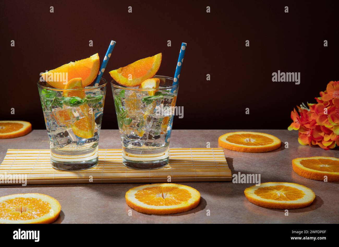 Deux cocktails dans un verre rempli de glace, feuilles de menthe garnies d'une tranche d'orange et sorbet sur serviette en bambou sur table en céramique avec orange s. Banque D'Images
