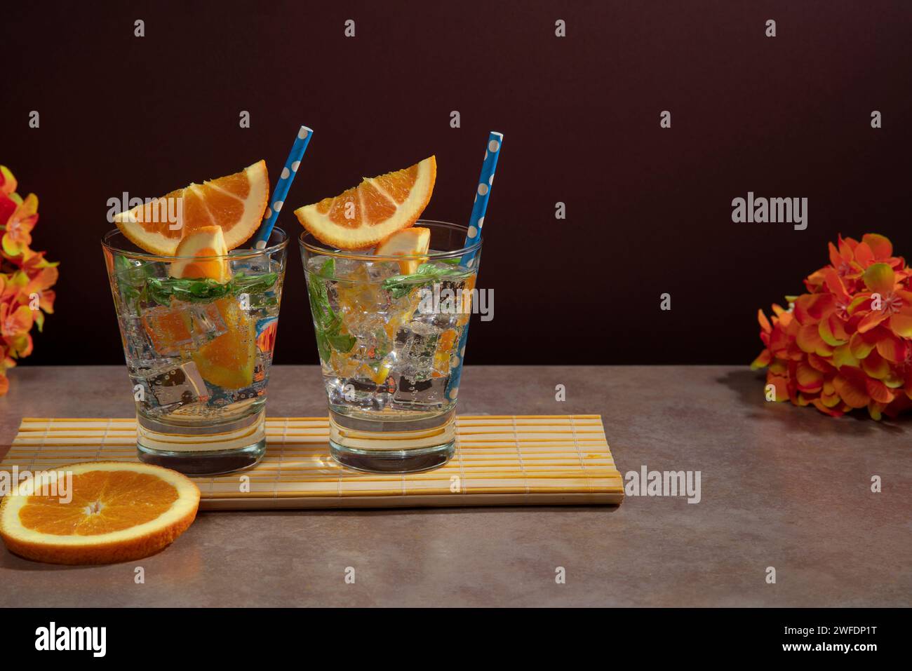 Deux cocktails en verre rempli de glace, feuilles de menthe garnies de tranche d'orange et sorbet sur serviette en bambou sur table en céramique avec un sli orange Banque D'Images