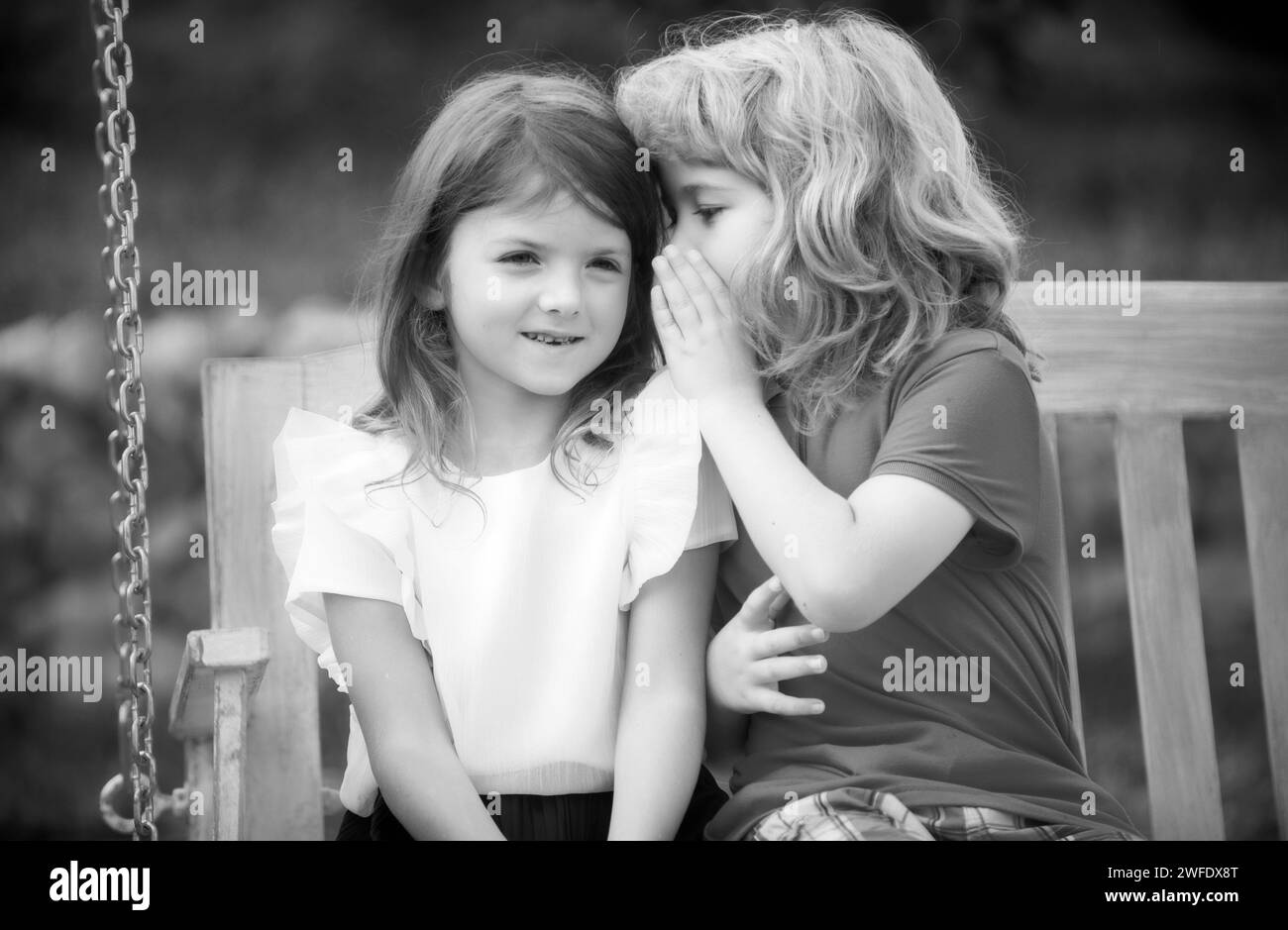 Un petit garçon murmure à une belle fille dans l'oreille. Frère et sœur jouant dans le parc printanier à l'extérieur. Un petit garçon et une petite fille s'amusent au printemps. Les enfants marchent Banque D'Images