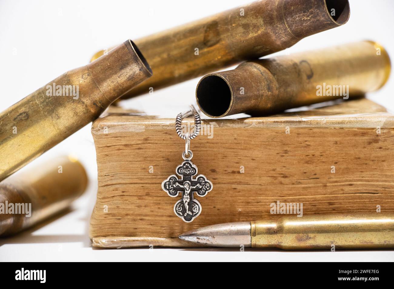 Cartouches vides, une balle, un livre et une croix en argent qui pèse sur un livre sur fond blanc, armes et religion, foi Banque D'Images