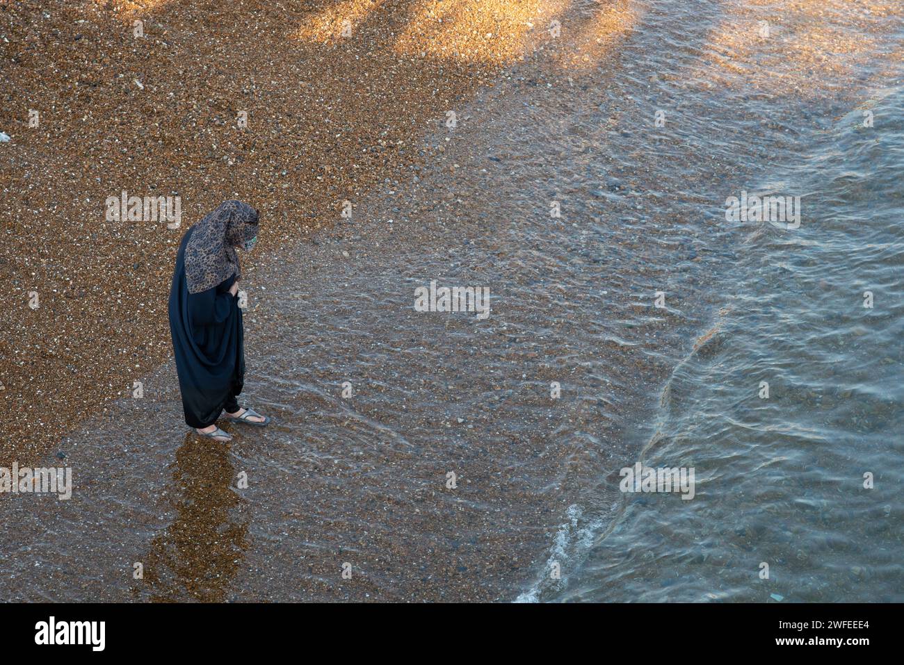 Femme musulmane arabe avec robe noire traditionnelle marchant sur la plage Banque D'Images