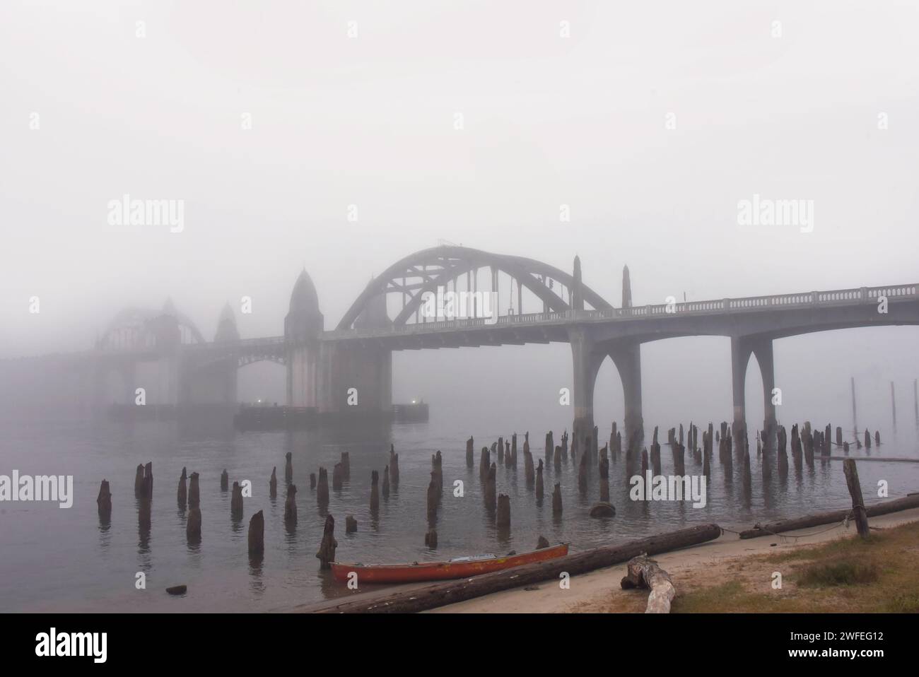 Le brouillard matinal recouvre le pont de la baie de Yaquina à Newport, Oregon. Le bateau de rangée rouge repose échoués en plus de pourrir, pilotis en bois. Banque D'Images
