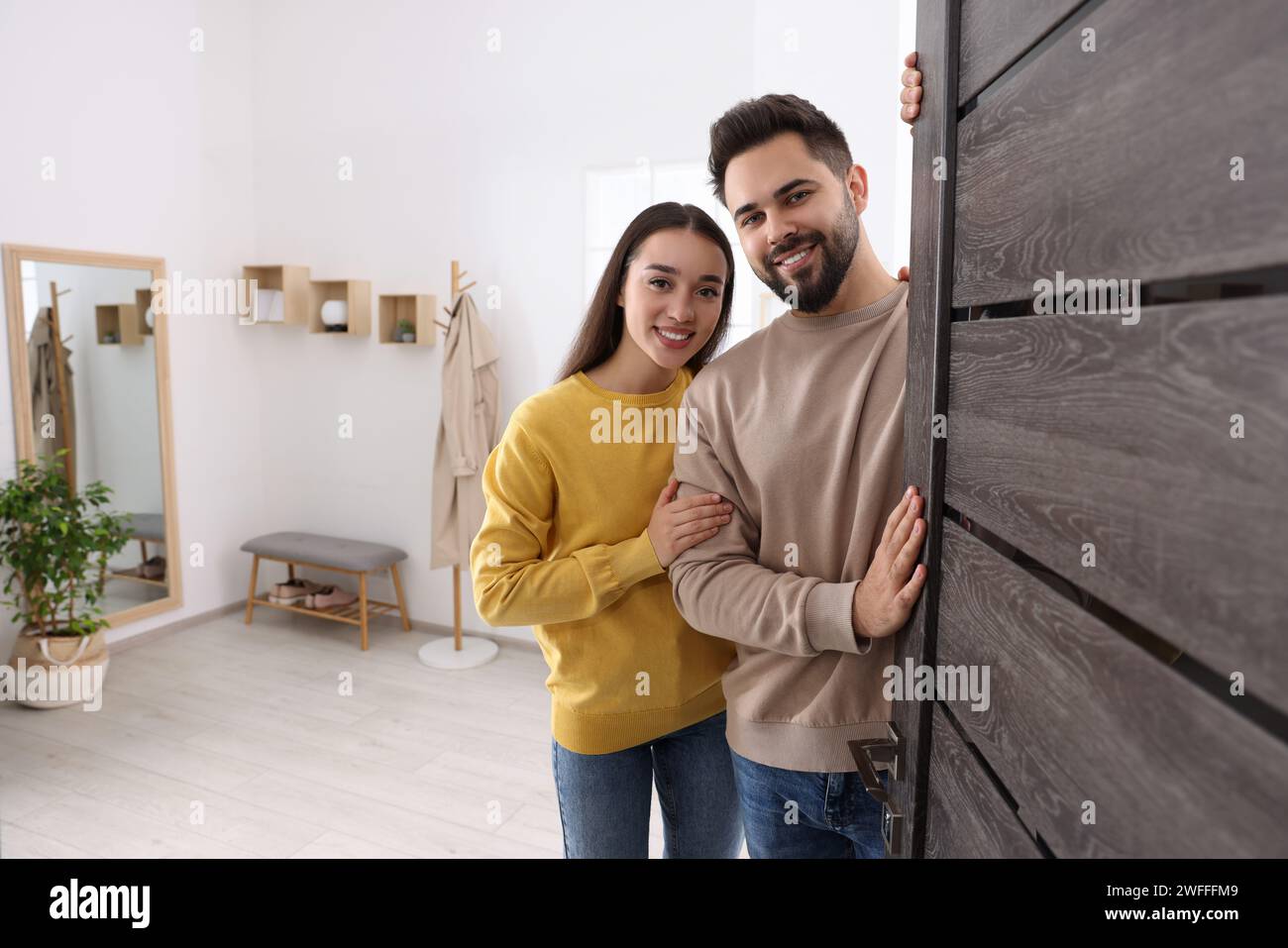 Couple heureux debout près de la porte, espace pour le texte. Invitation à venir à l'intérieur Banque D'Images