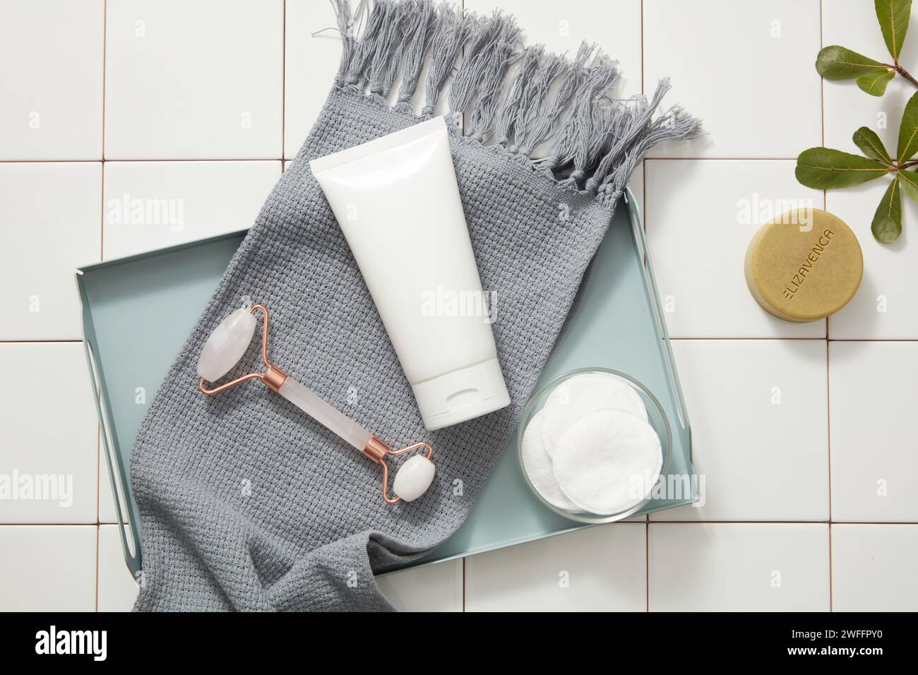 Un rouleau de massage facial en quartz rose, un tube blanc et une serviette placés sur un plateau rectangulaire avec des tampons de coton. Le concept de crème ou de produits hydratants Mo Banque D'Images