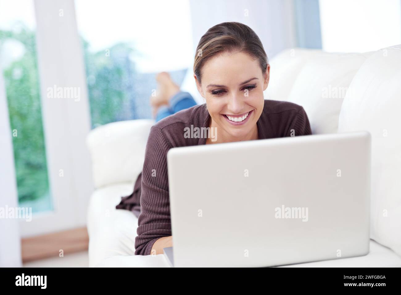 Femme, ordinateur portable et se détendre sur le canapé pour le travail à distance, des films en streaming et mise à jour de blog à la maison. Heureux freelance, ordinateur et abonnement de téléchargement Banque D'Images