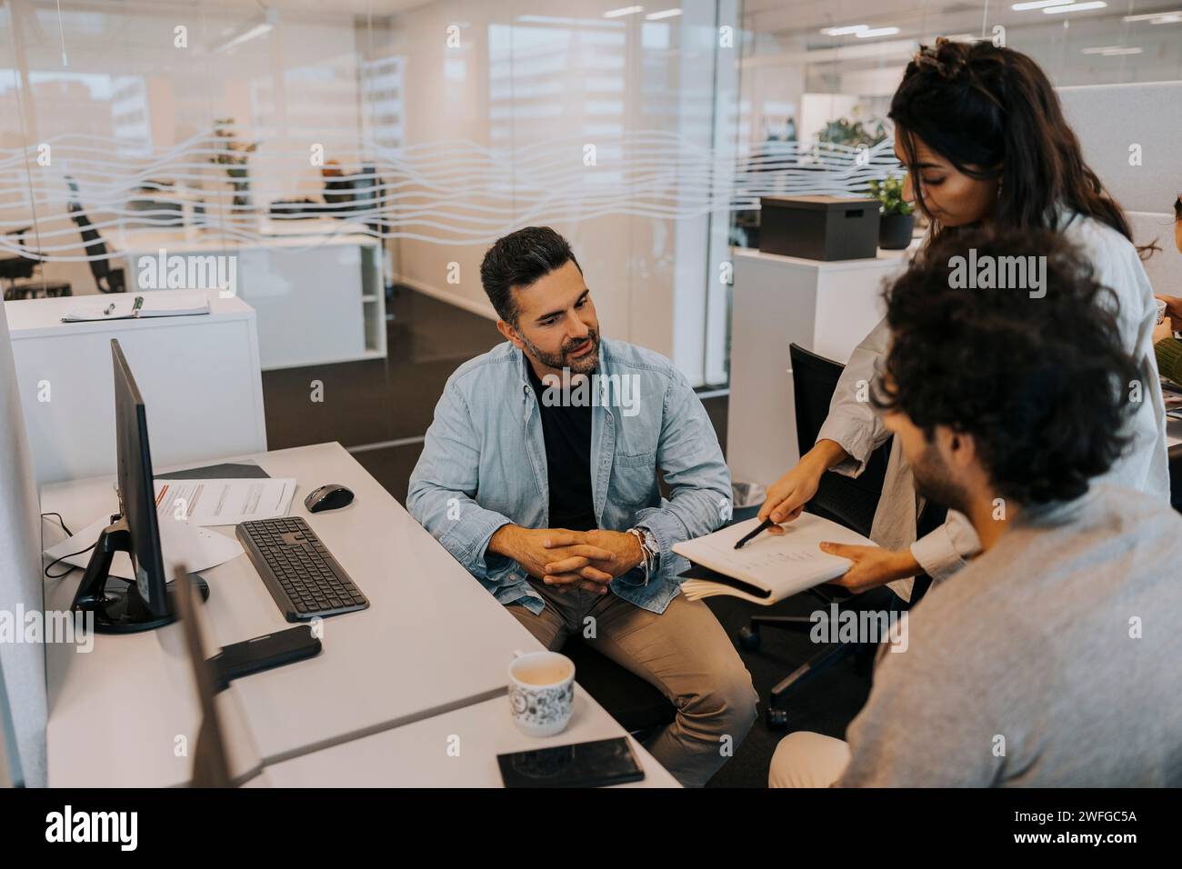 Jeune femme d'affaires montrant la stratégie à des collègues masculins tout en discutant au bureau Banque D'Images