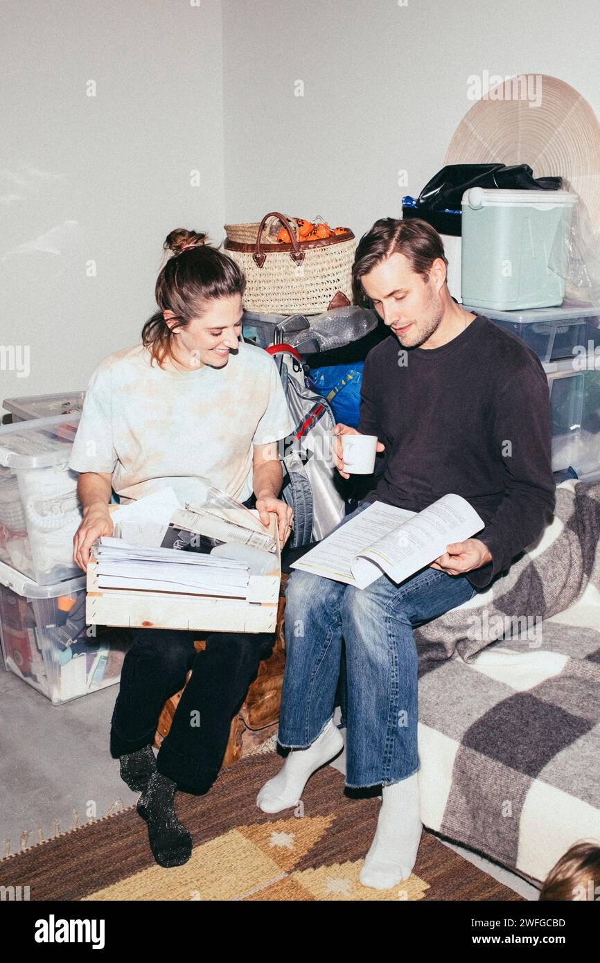 Couple lisant le livre tout en étant assis pendant le déménagement de la maison Banque D'Images