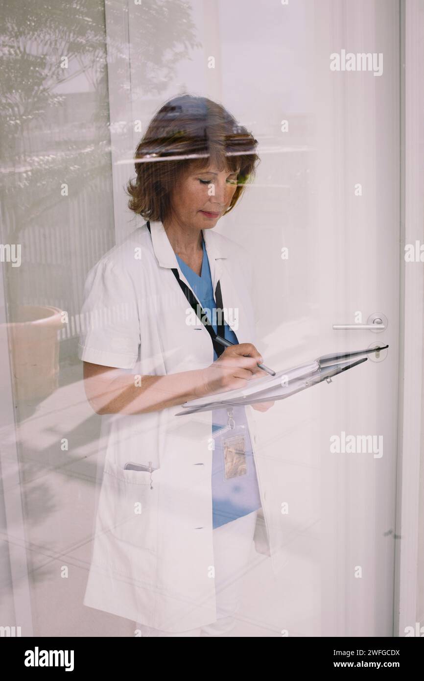 Médecin senior examinant le dossier médical vu à travers le verre Banque D'Images Médecin senior examinant le dossier médical vu à travers le verre Banque D'Images