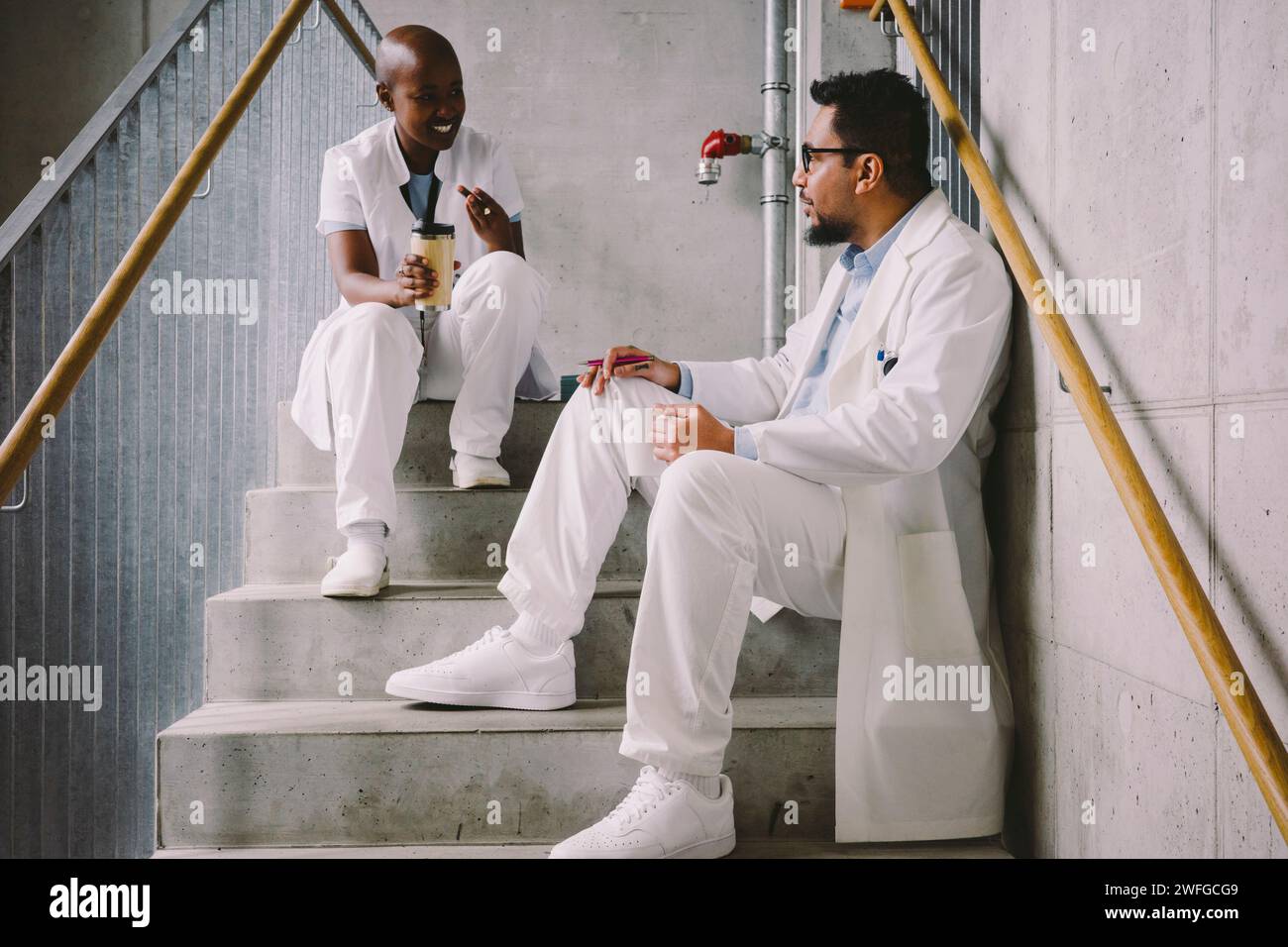 Heureux collègues médicaux parlant en étant assis à l'escalier pendant la pause café Banque D'Images