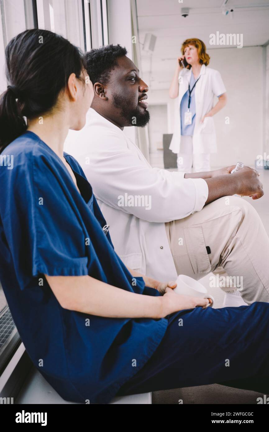 Vue latérale des collègues médicaux masculins et féminins assis à la cafétéria de l'hôpital Banque D'Images