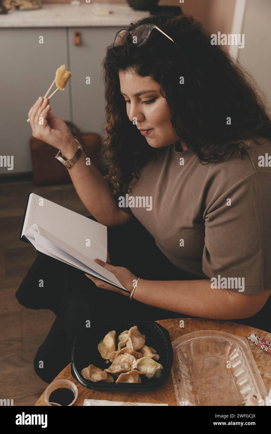 Femme d'affaires mangeant des boulettes tout en lisant le journal au bureau Banque D'Images