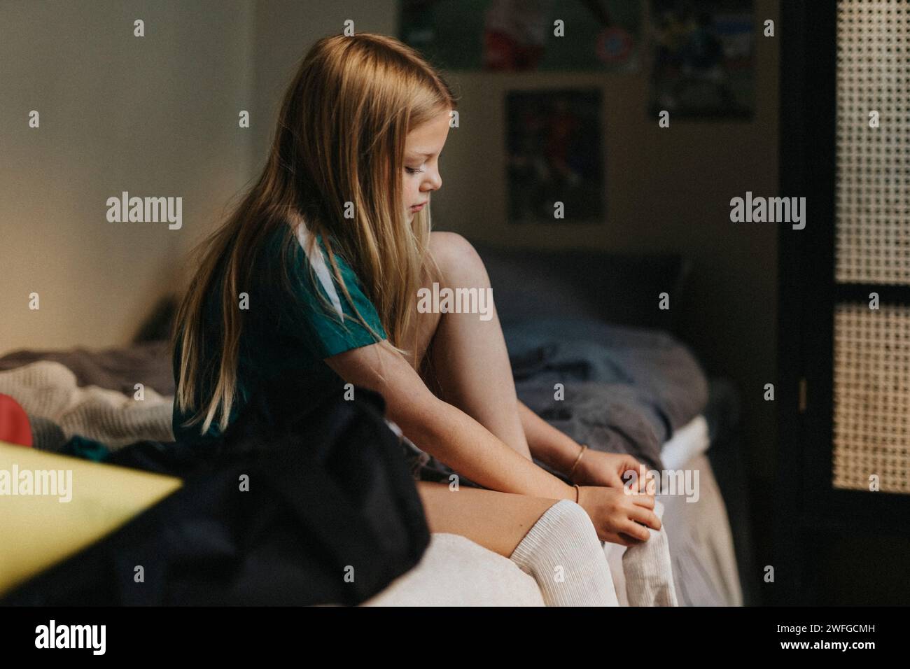 Fille élémentaire blonde portant une chaussette tout en étant assise sur le lit à la maison Banque D'Images