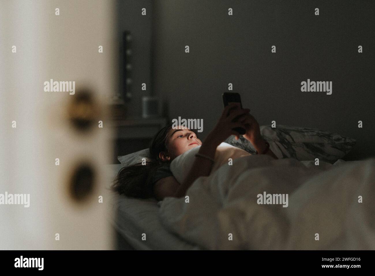 Fille utilisant le téléphone portable tout en étant couché sur le lit dans la chambre à coucher à la maison intelligente Banque D'Images
