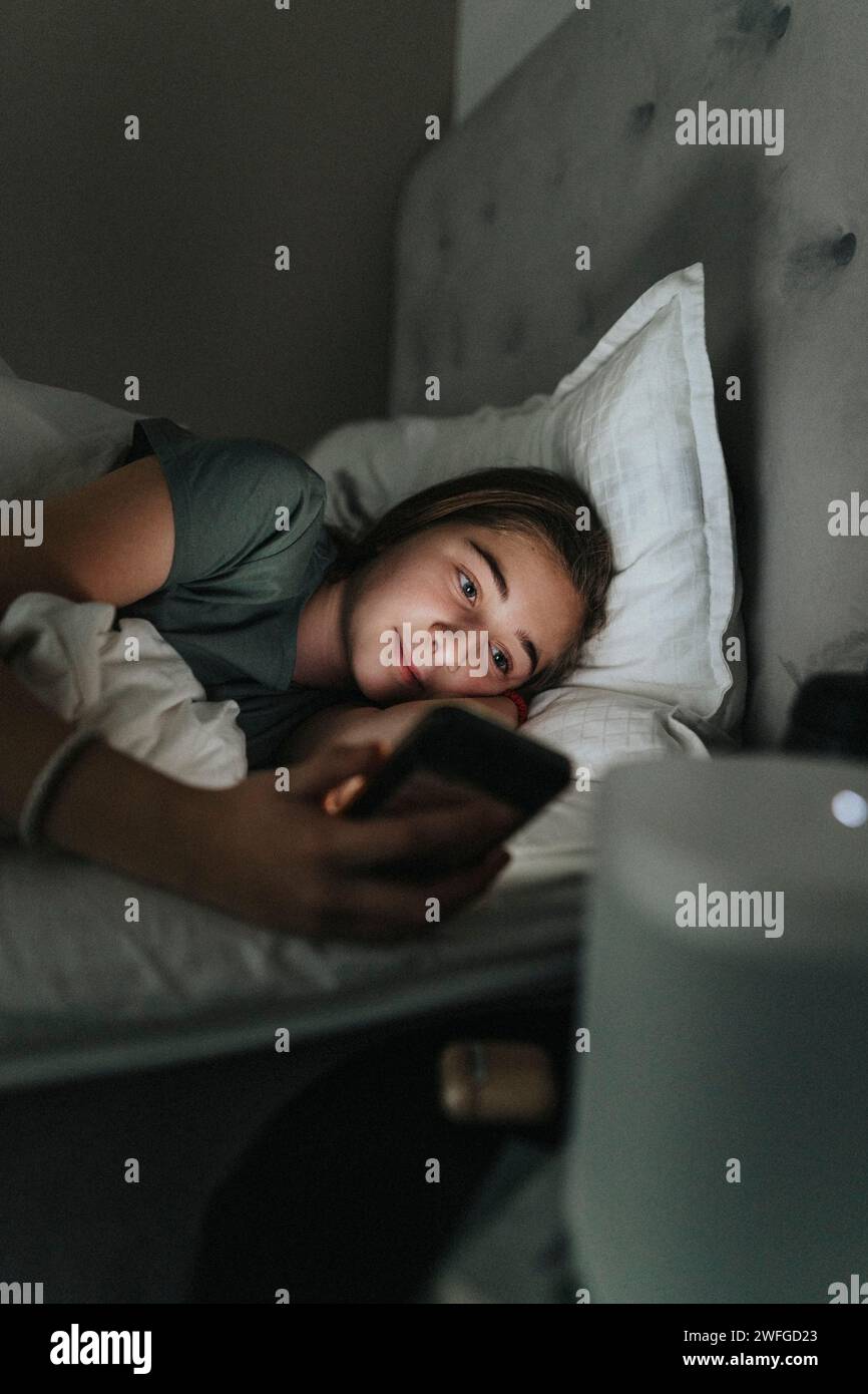 Fille pré-adolescente utilisant un téléphone portable tout en étant couché sur le lit dans la chambre à coucher à la maison intelligente Banque D'Images