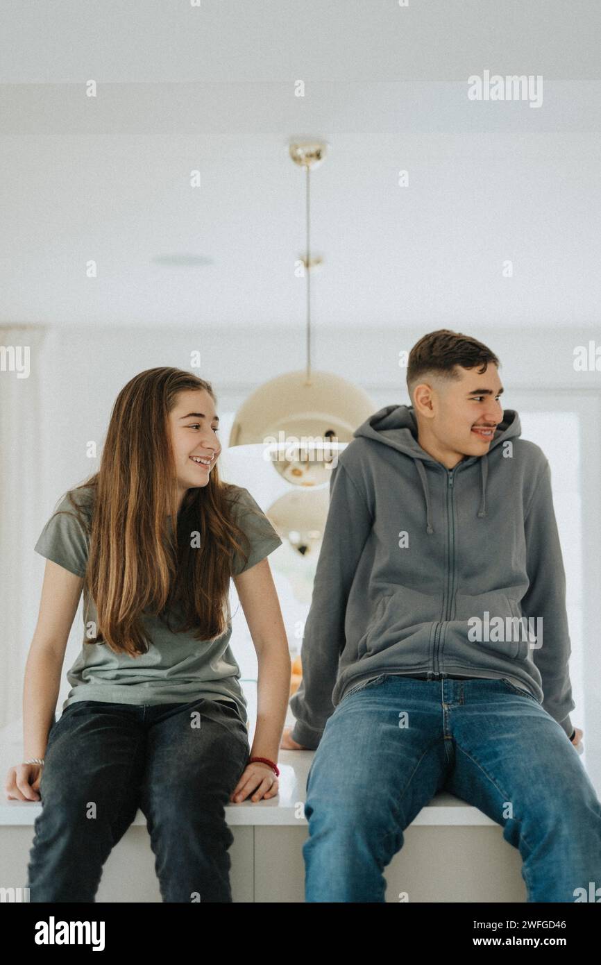 Frères et sœurs souriants assis sur l'îlot de cuisine à la maison Banque D'Images