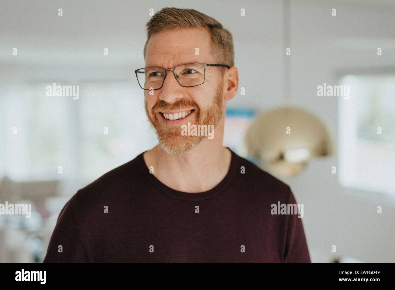 Homme mûr souriant portant des lunettes regardant loin à la maison moderne Banque D'Images